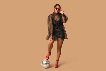 Poster - Stylish young African-American woman with dreadlocks and disco ball on brown background