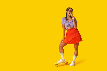 Sticker - Beautiful young African-American woman with dreadlocks holding lollipop and skateboard on yellow background