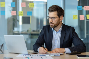 Wall Mural - Focused businessman working on laptop in modern office setting