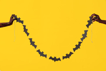 Poster - Hands of zombies with garland made of paper bats on yellow background. Halloween celebration