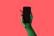 © Pixel-Shot - Green hand of witch with mobile phone on red background. Halloween celebration