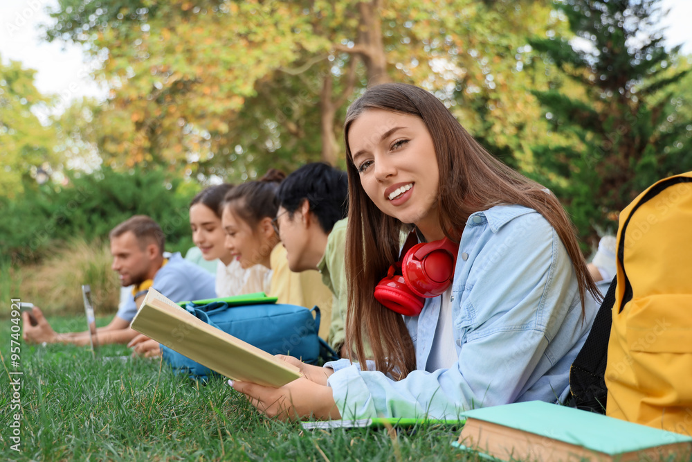 Female student with book and her classmates lying on grass in park