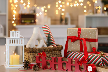 Wall Mural - Beautiful gift boxes with packing materials and decorations on table against glowing garland at home, closeup