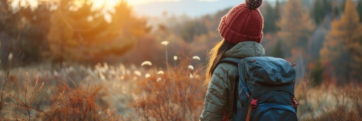 Canvas Print - Woman hiking in a vibrant autumn forest with a backpack and knitted hat while appreciating the sunrise during the fall season.