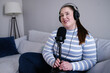© Oleksii Syrotkin/Stocksy - Female content maker sitting on sofa during podcast broadcasting