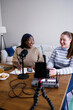 © Oleksii Syrotkin/Stocksy - Two smiling multiracial women recording podcast at home office