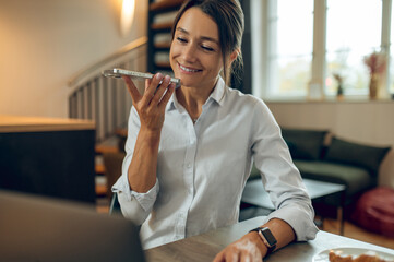 Smiling young caucasian woman recording an audio message and looking contented