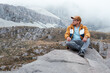 © J Esteban Berrío/Stocksy - Tourist sitting on a rock in the midst of a cold and rocky landscape