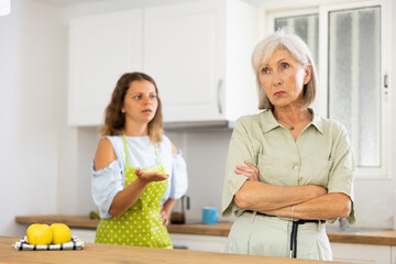 Wall Mural - Sad senior woman ignoring her daughter standing in background and arguing with her.