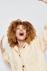 joyful woman expressing happiness with curly hair in a cozy sweater against a bright white background, conveying energy and positivity, ideal for lifestyle and wellness themes