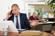 © JackF - Dissatisfied irritated businessman emotionally talking on mobile phone while sitting at office table with laptop