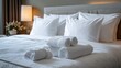 © Puttipong - A bed in a luxurious hotel room, with crisp white linens, perfectly arranged pillows, and a folded towel on the bed.