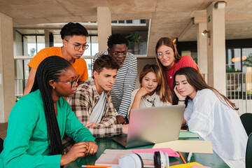 Large team of international young students using a laptop, collaborating on college research task in university campus library. Cooperation of teenagers finding data on notebook for a high school task