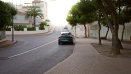 Wall Mural - Blurred streetscape featuring a parked car, trees, and residential buildings under soft, natural light, captured with a bokeh effect on a clear day.