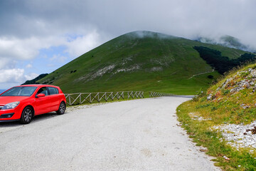 Wall Mural - Picturesque view of green forest and red car in mountains