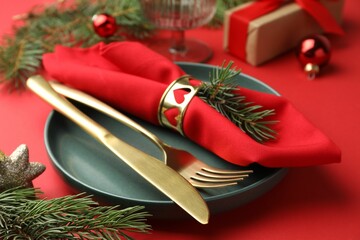 Poster - Beautiful Christmas setting with plate, elegant cutlery and festive decor on red table, closeup