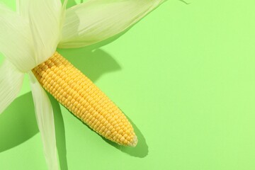 Poster - Fresh ripe corncob with husks on light green background, top view. Space for text