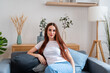 © mahalo studio/Stocksy - redhead woman sitting on sofa
