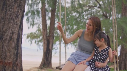 Wall Mural - Asian young daughter sitting on wooden swing at the beach with mommy. 