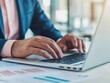 © kokoson6 - Close-up of businessman's hands typing on laptop keyboard, working on project in office.