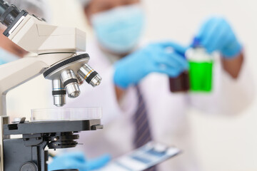 two asian scientists in lab coats sit at a table in a laboratory, examining samples through a micros