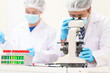 © NanSan - Two Asian scientists in lab coats sit at a table in a laboratory, examining samples through a microscope. The room is equipped with scientific tools, liquids, and chemistry materials.