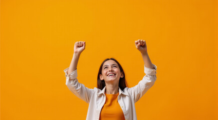 Excited woman in a pink blazer celebrating success while talking on the phone against a bright orange background