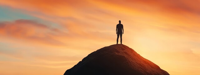  A man atop a mountain as the sun sets, backdropped by clouds in the sky