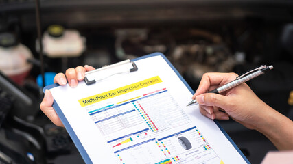 Close-up at a mechanic foreman's hand is checking on multi-point car service guideline checklist form, to verify the car service quality. Expertise working action scene, selective focus.