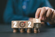 © Nirusmee - Businessman hand flipping wooden block cube from 2024 to 2025 on coins stacking for setup objective target business cost and budget planing of new year concept.
