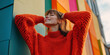 © HelgaQ - Joyful woman in vibrant orange sweater smiling against colorful wall background