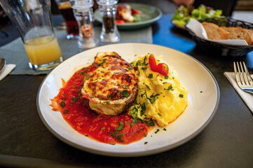 Grilled eggplant with cheese in tomato sauce with mashed potato, drink, and many things on restaurant table.