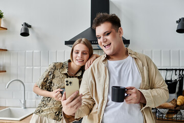 Friends share a joyful moment, sipping coffee and browsing on their phone in the kitchen.