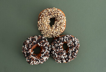 donuts with sprinkles of white, milk and dark chocolate balls on a green background, not a healthy diet, fatty and junk food, sweet pastries, donut day, Fat Thursday
