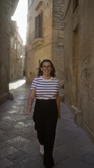 Wall Mural - Smiling woman in black and white attire walking down a narrow, sunlit italian street in lecce, puglia.