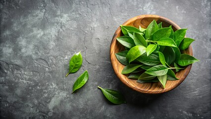 Wall Mural - A wooden bowl filled with green leaves on a gray surface with a leafy branch