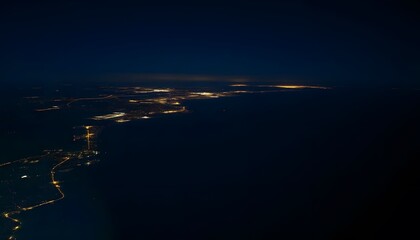 Wall Mural - Aerial view of a coastal city at night, with a winding road and scattered lights illuminating the landscape against a dark background