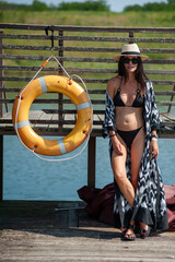 Wall Mural - beautiful girl in a black swimsuit with a hat and sunglasses on the background of the sea