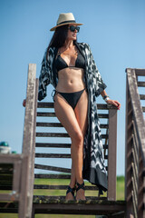 Wall Mural - beautiful girl in a black swimsuit with a hat and sunglasses on the background of the sea