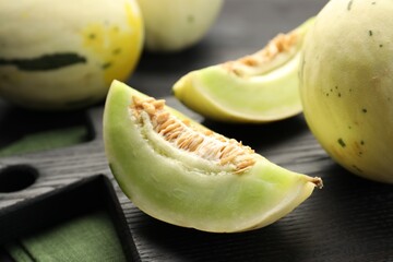 Fresh whole and cut honeydew melons on black wooden table, closeup