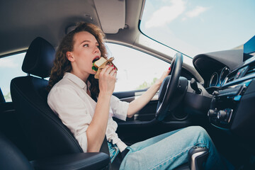 Poster - Photo of cheerful pretty lady dressed white shirt smiling driving rented automobile eating snack outdoors urban city street