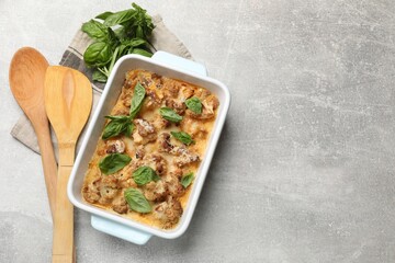 Poster - Tasty baked cauliflower in baking dish and basil on light grey table, top view. Space for text