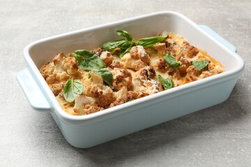 Canvas Print - Tasty baked cauliflower and basil in baking dish on light grey table, closeup