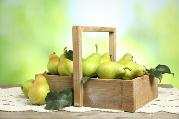 Crate with fresh pears and leaves on wooden table against blurred green background, closeup