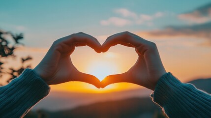 A close-up of hands forming a heart shape against a beautiful sunset background