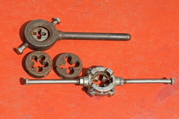 set of rusty iron industrial mechanical hand old round different dies for cutting threads for bolts with keys lie on a dirty red  table outdoors