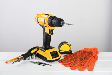 Sticker - Cordless electric drill, gloves, bits, screwdriver and measuring tape on white wooden table