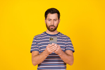 Poster - Portrait of serious guy with bristle wear striped t-shirt look at smartphone read notification isolated on vivid yellow color background