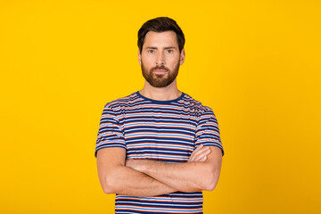 Wall Mural - Portrait of handsome confident experienced master businessman in striped t shirt crossed hands isolated on yellow color background