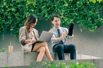 A male and female business team engage in discussion utilizing a laptop and notes. team sitting at outdoor pedestrian landscape. reflecting the importance of collaboration and strategic planning.